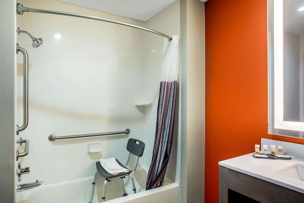 A bathroom with a shower, grab bars, a chair, and a sink with toiletries.