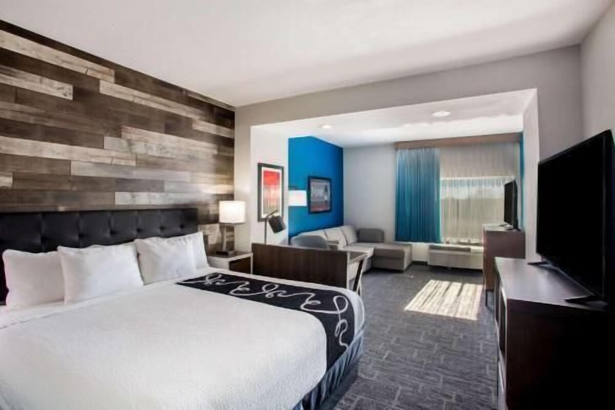 A hotel room with a bed, a desk, a chair, a TV, and a window with curtains.