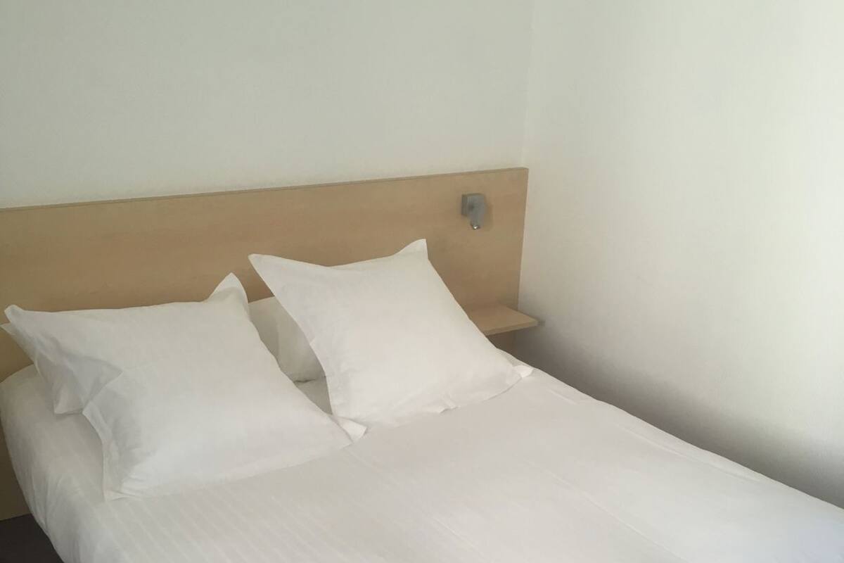 Uma cama com roupa de cama branca, cabeceira de madeira e mesa de cabeceira com abajur.