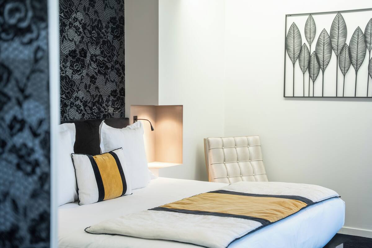 Quarto de hotel com cama, poltrona, obra de arte na parede e parede estampada.