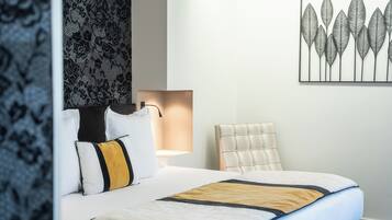 A hotel room with a bed, a chair, a wall-mounted artwork, and a patterned wall.