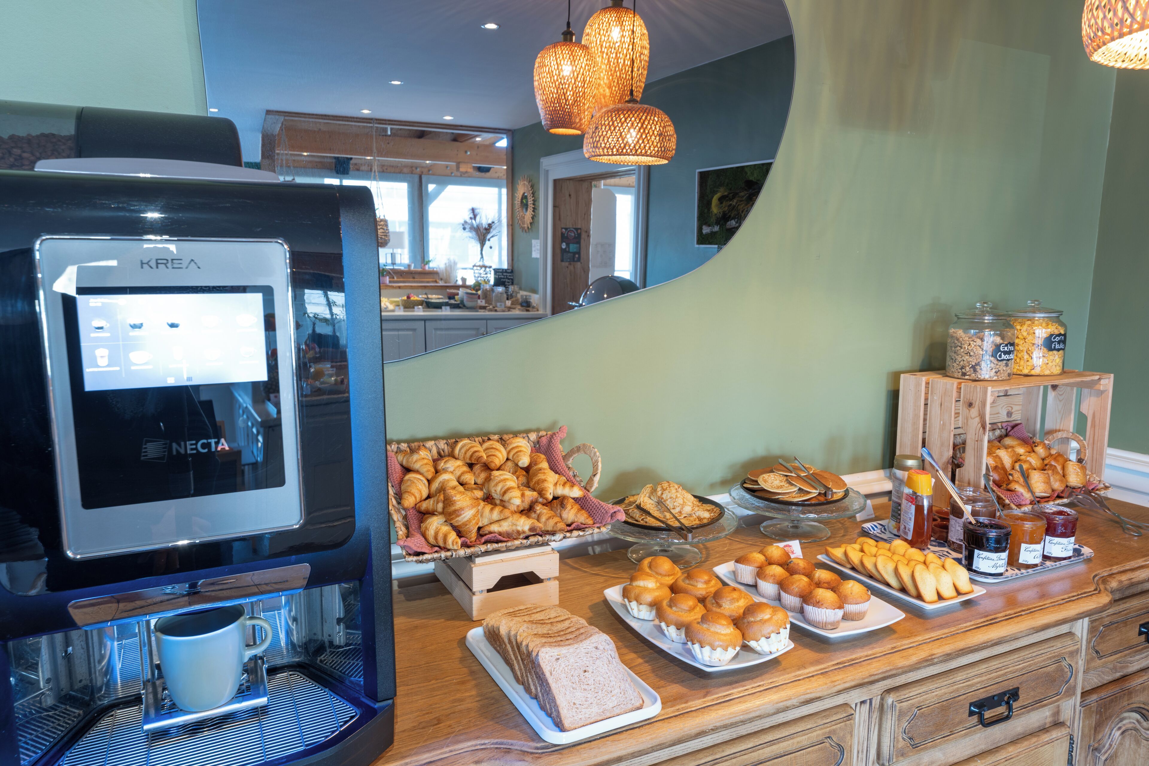 A coffee station with a KREA coffee machine, pastries, and a buffet with bread and muffins.