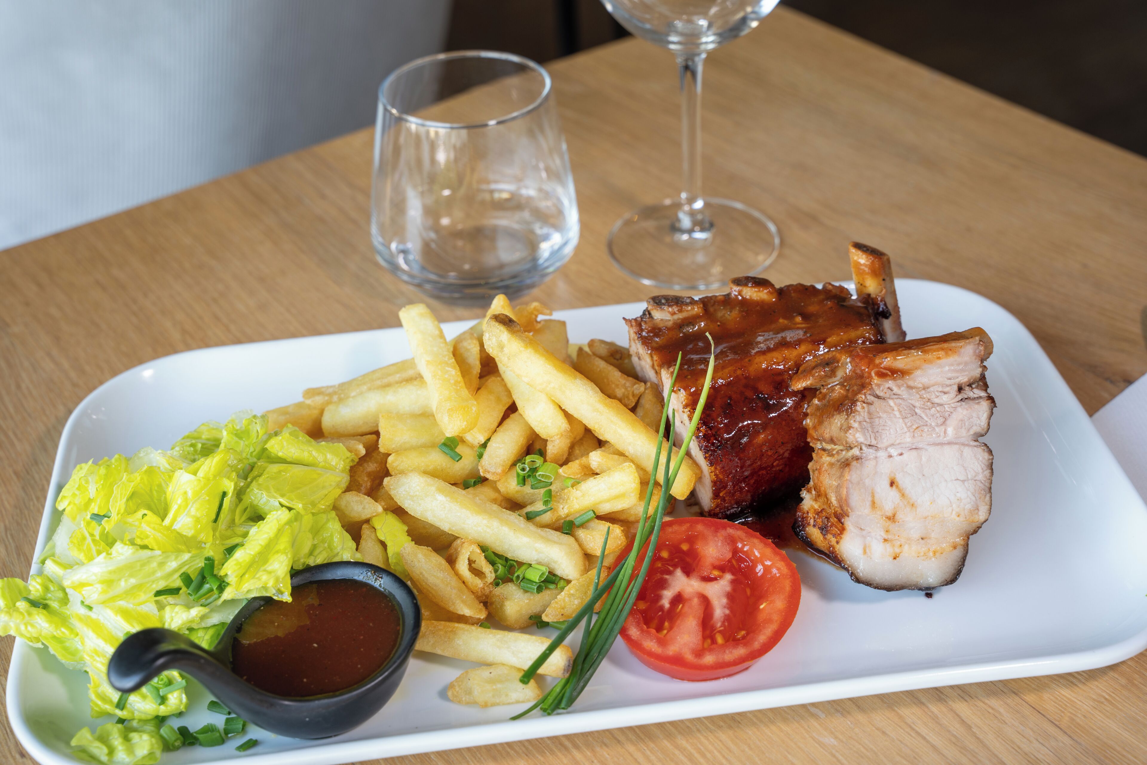 A plate of food with ribs, fries, lettuce, and a tomato.