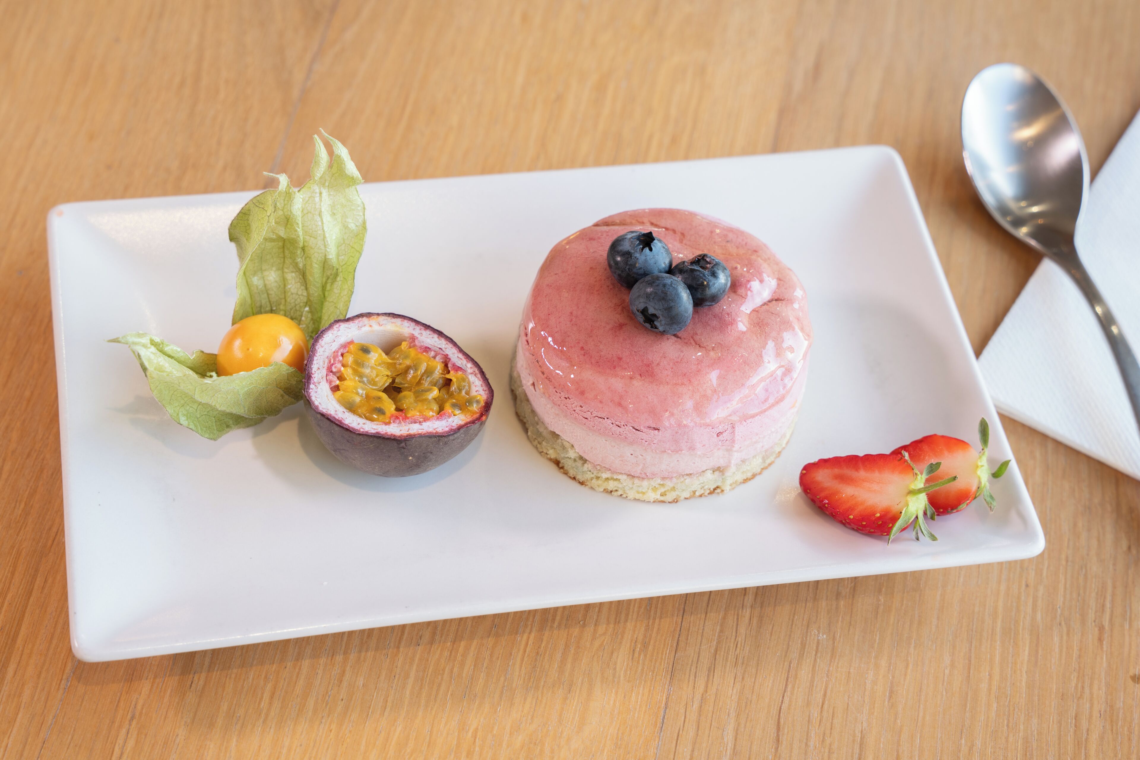 A dessert plate with a round cake, passion fruit, and a strawberry.