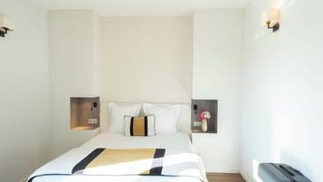 Una camera d'albergo con un letto, comodini, una lampada a parete e una valigia.