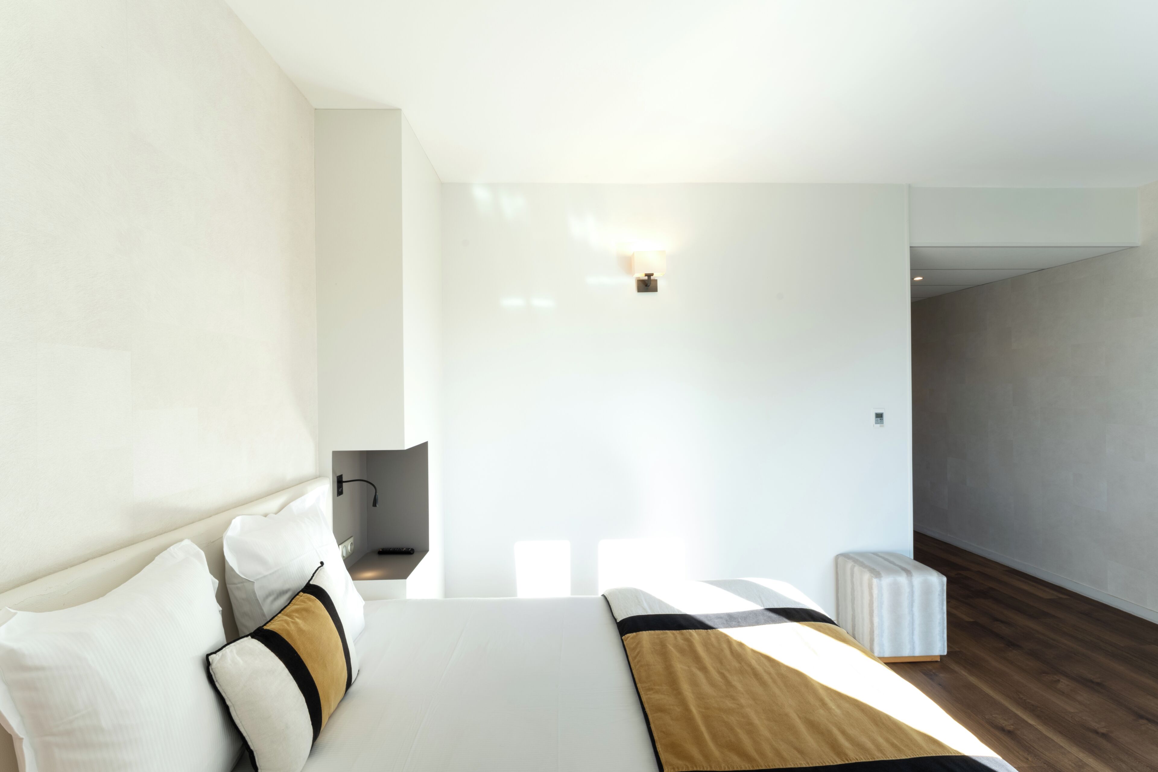Una habitación de hotel moderna con una cama grande, una mesita de noche, una silla y un pequeño reposapiés.