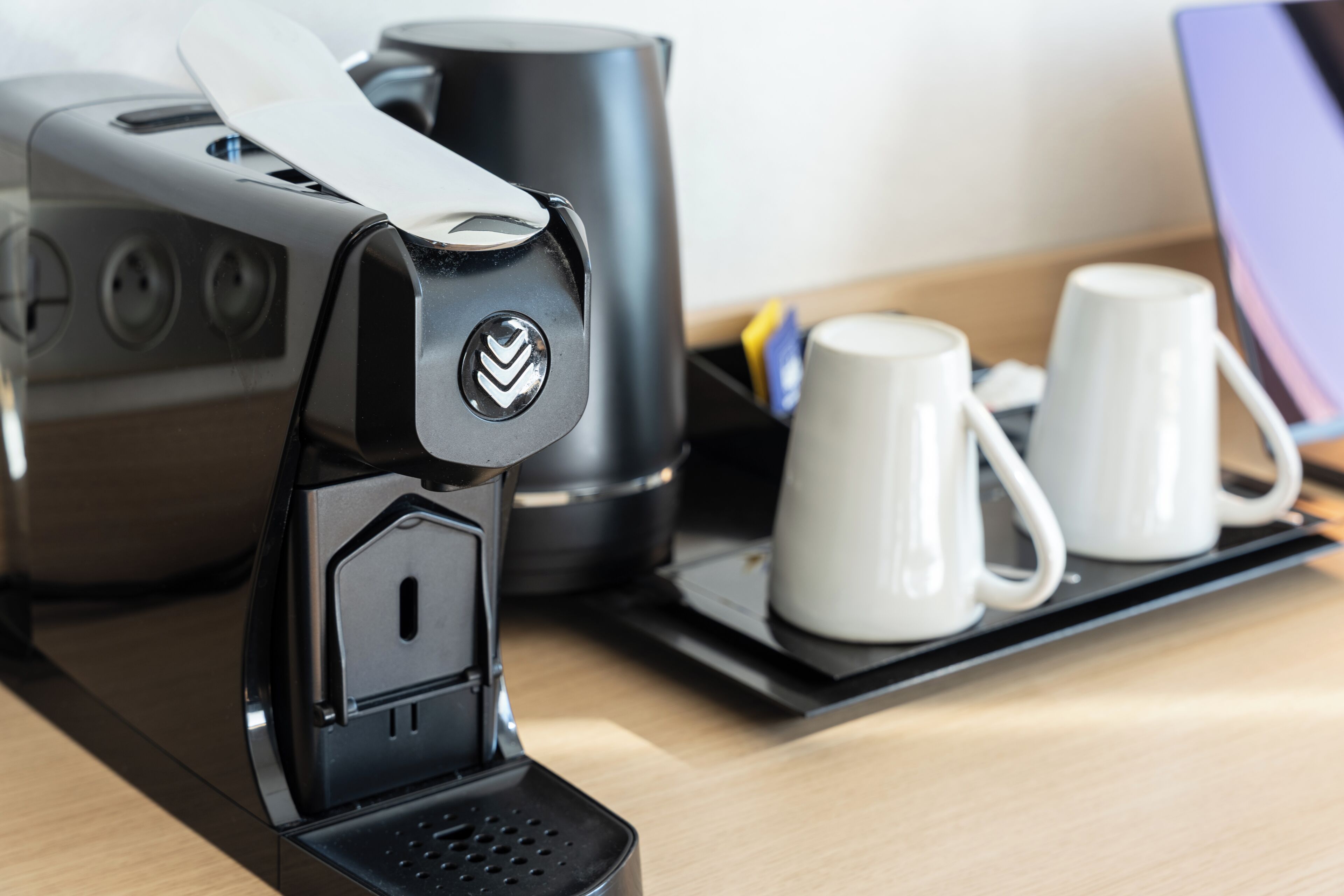 Una cafetera con un panel de control, una jarra de café negro y dos tazas blancas sobre una bandeja.