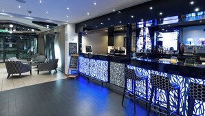 A modern bar area with a patterned light-up partition, bar stools, and a seating area with patterned chairs.