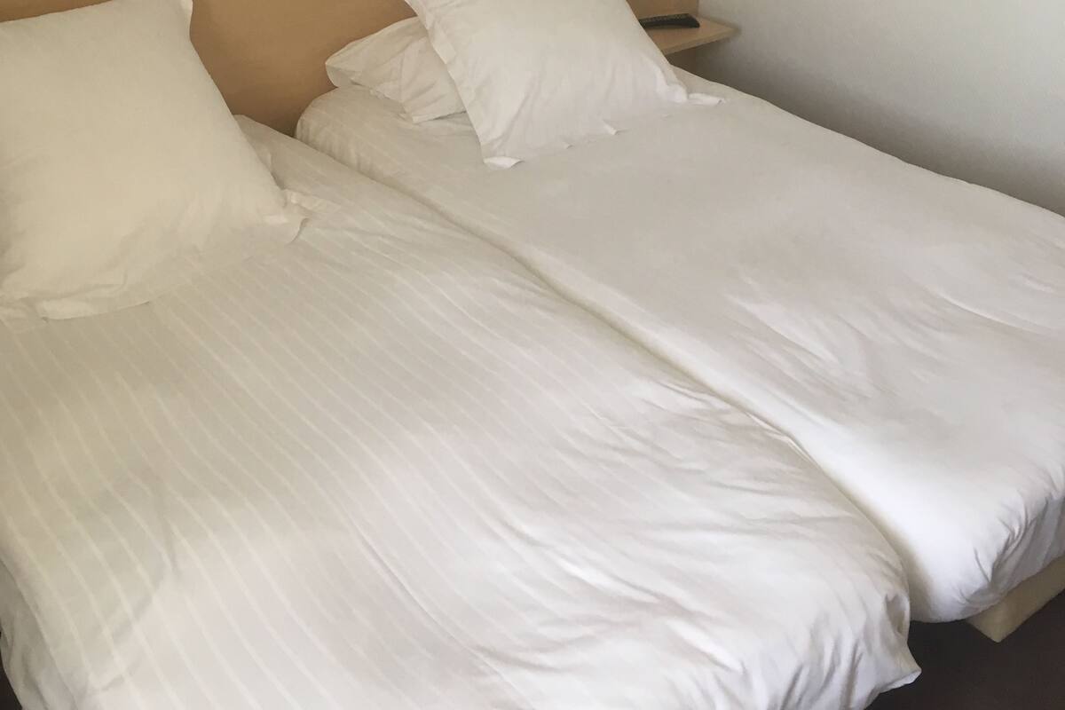 Uma cama de casal com roupa de cama branca, cabeceira de madeira e mesa de cabeceira com abajur.