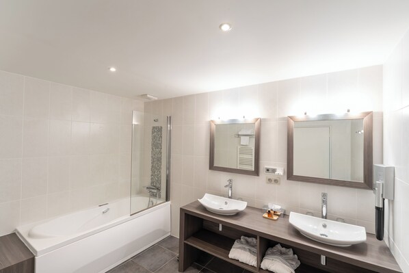 A modern bathroom with a bathtub, two sinks, and a large mirror. - Le Konine Suites (Montceau-les-Mines)