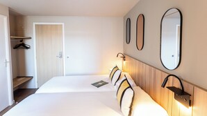 A hotel room with a bed, a mirror, and a wall-mounted light fixture.