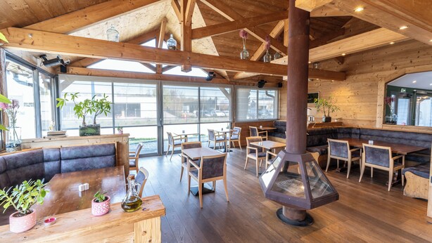 A restaurant with wooden beams, large windows, and a central wood stove.