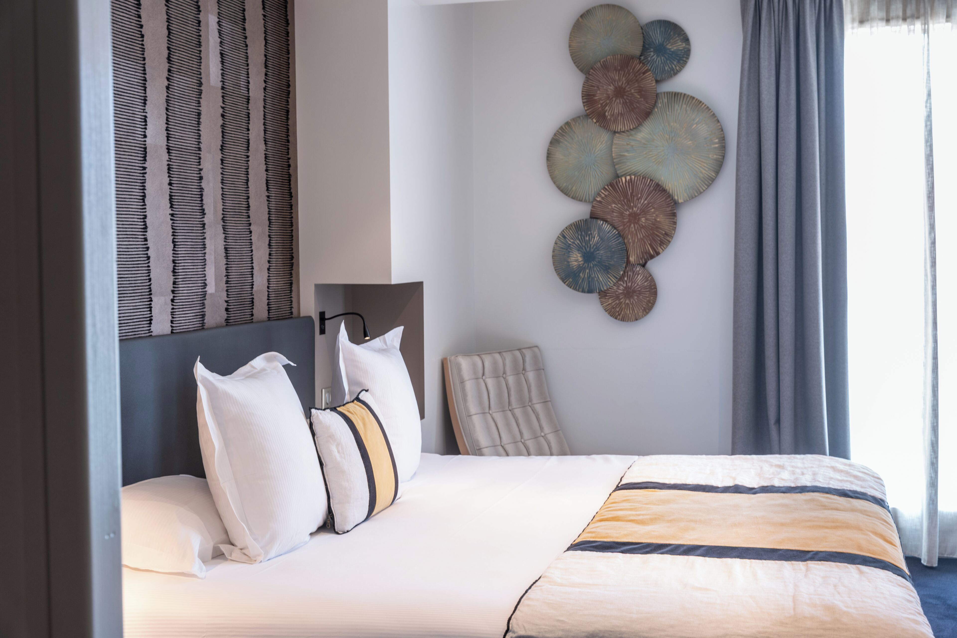 A modern hotel room with a neatly made bed, a headboard, and a wall with decorative plates.