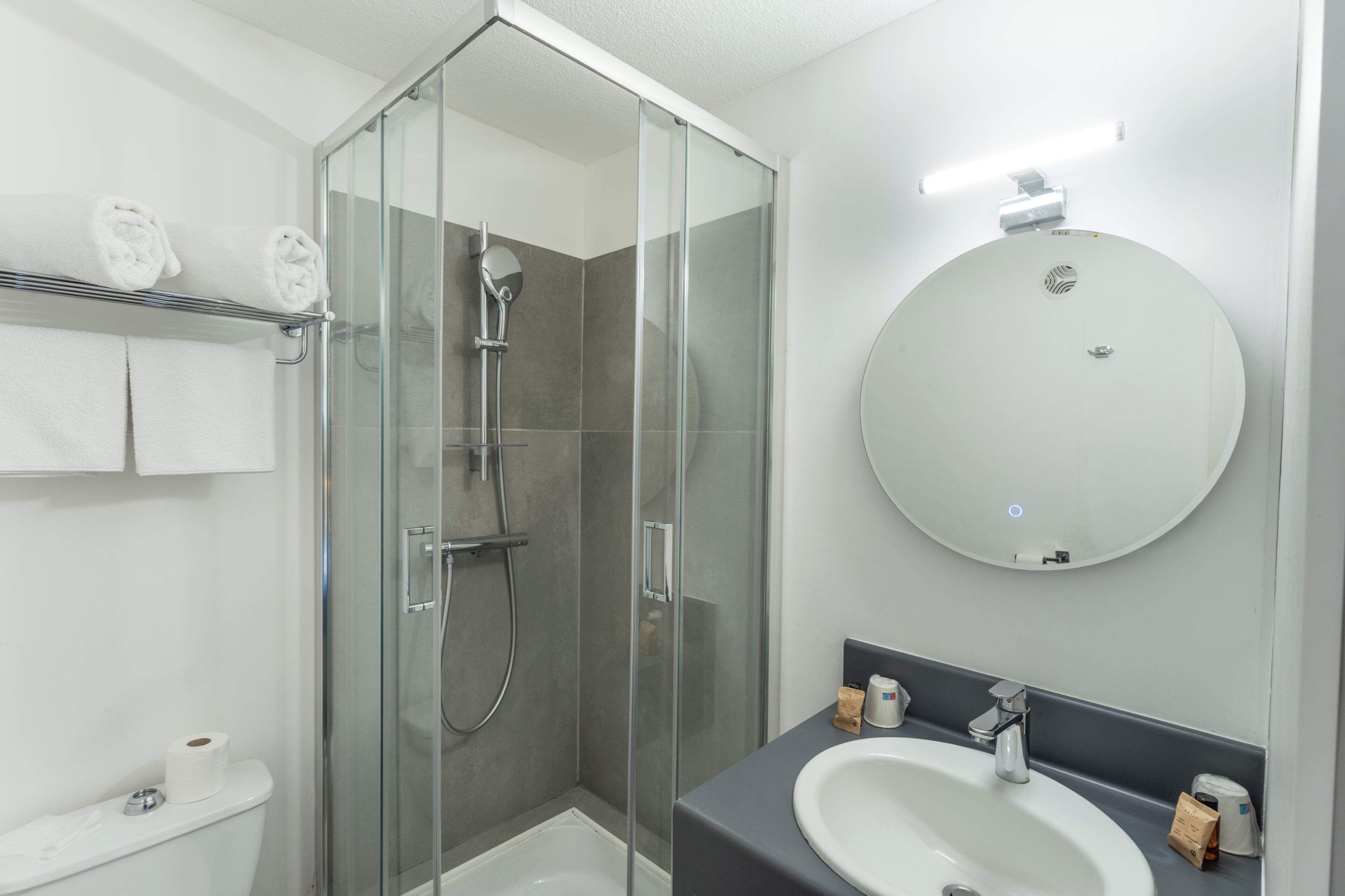 A modern bathroom with a glass-enclosed shower, a round mirror, and a white sink.