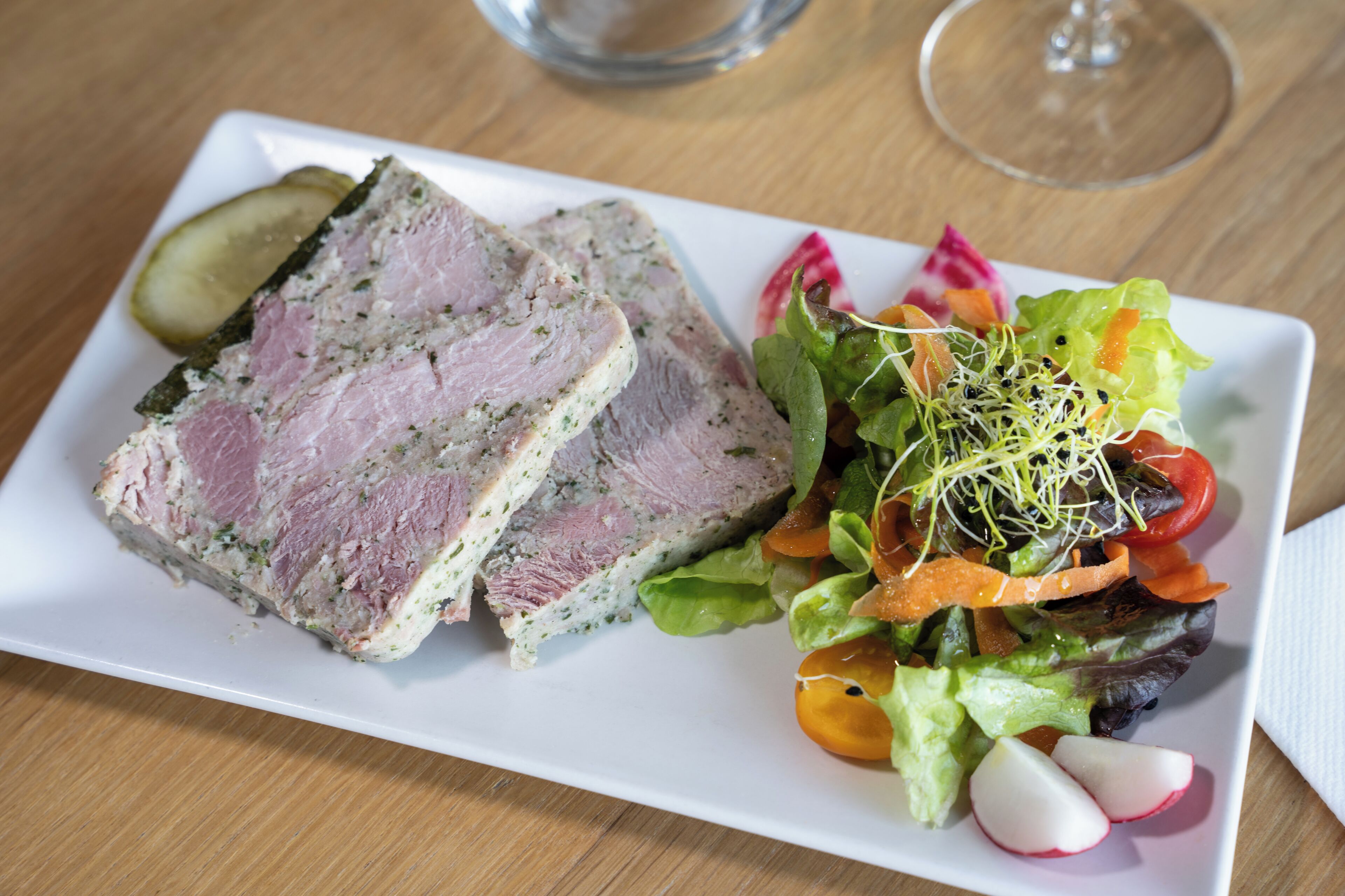 Ein weißer, rechteckiger Teller mit geschnittenem Fleisch und einem gemischten Gemüsesalat.