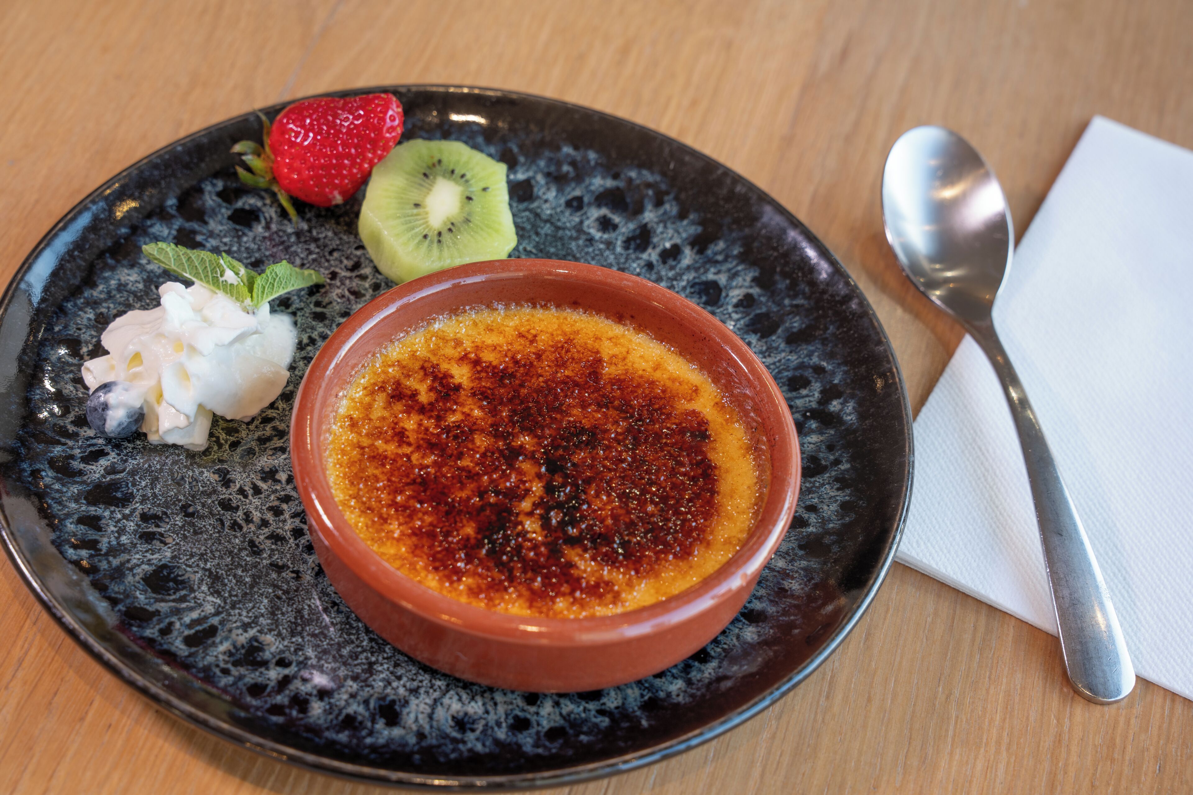Ein Dessertteller mit Crème brûlée, Kiwi, Erdbeere und Schlagsahne.