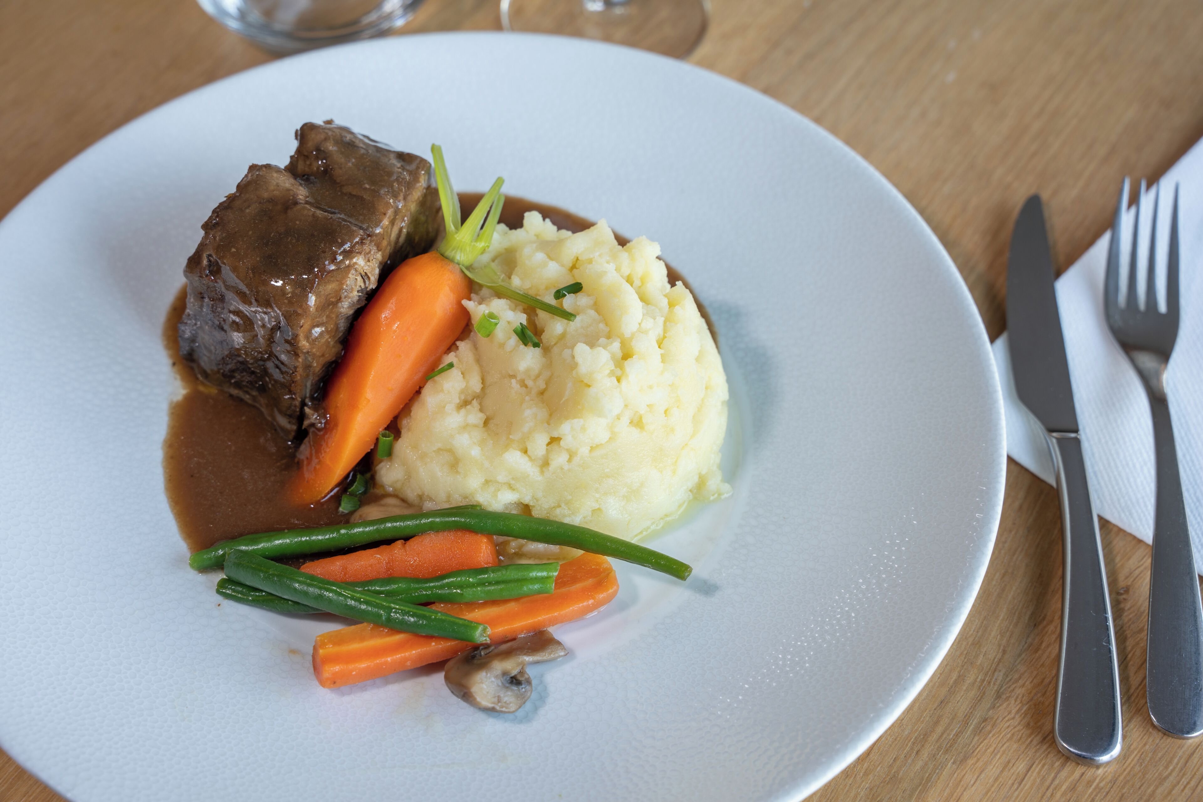 A plate with beef, mashed potatoes, carrots, and green beans.