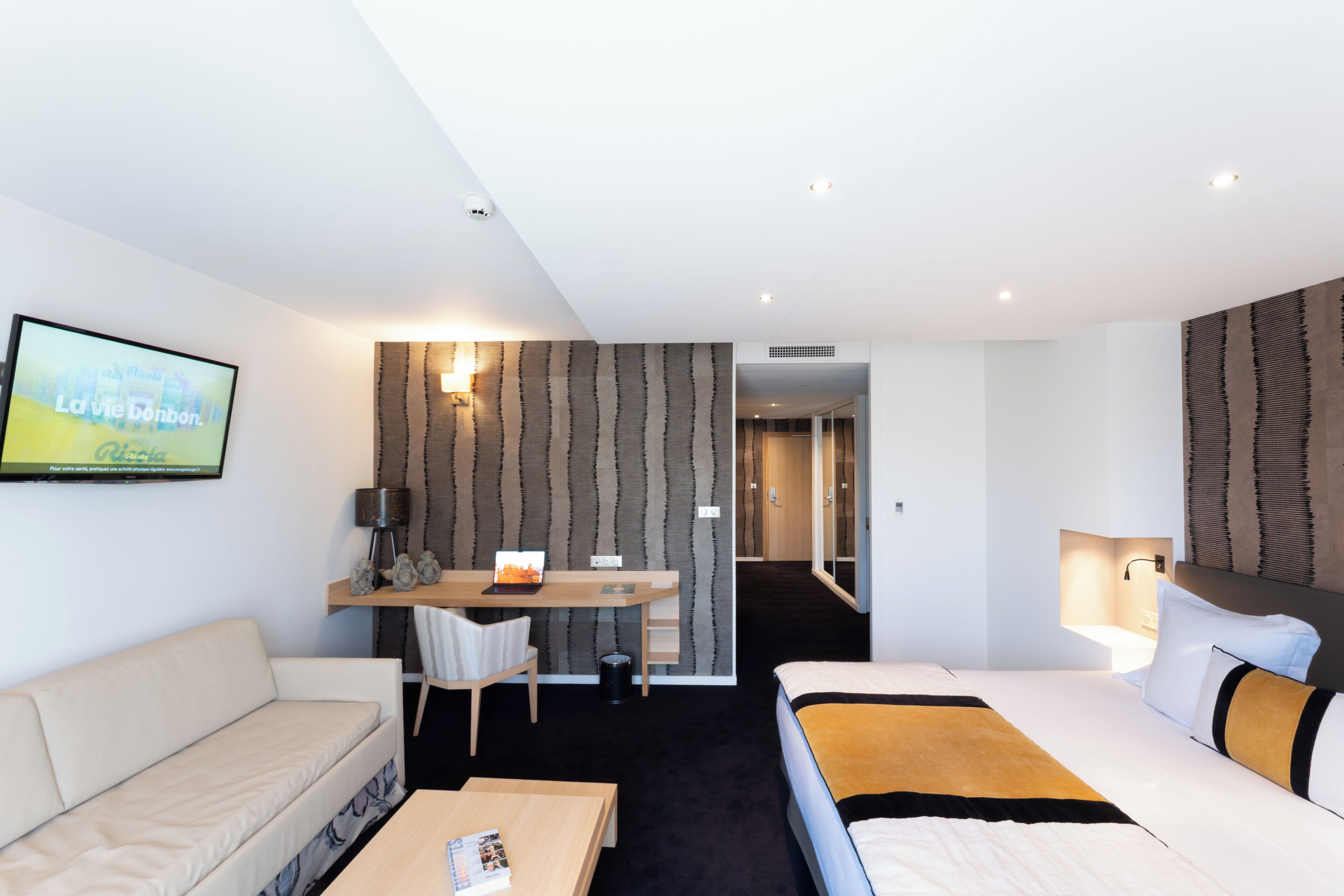 A hotel room with a bed, a sofa, a desk, and a TV.