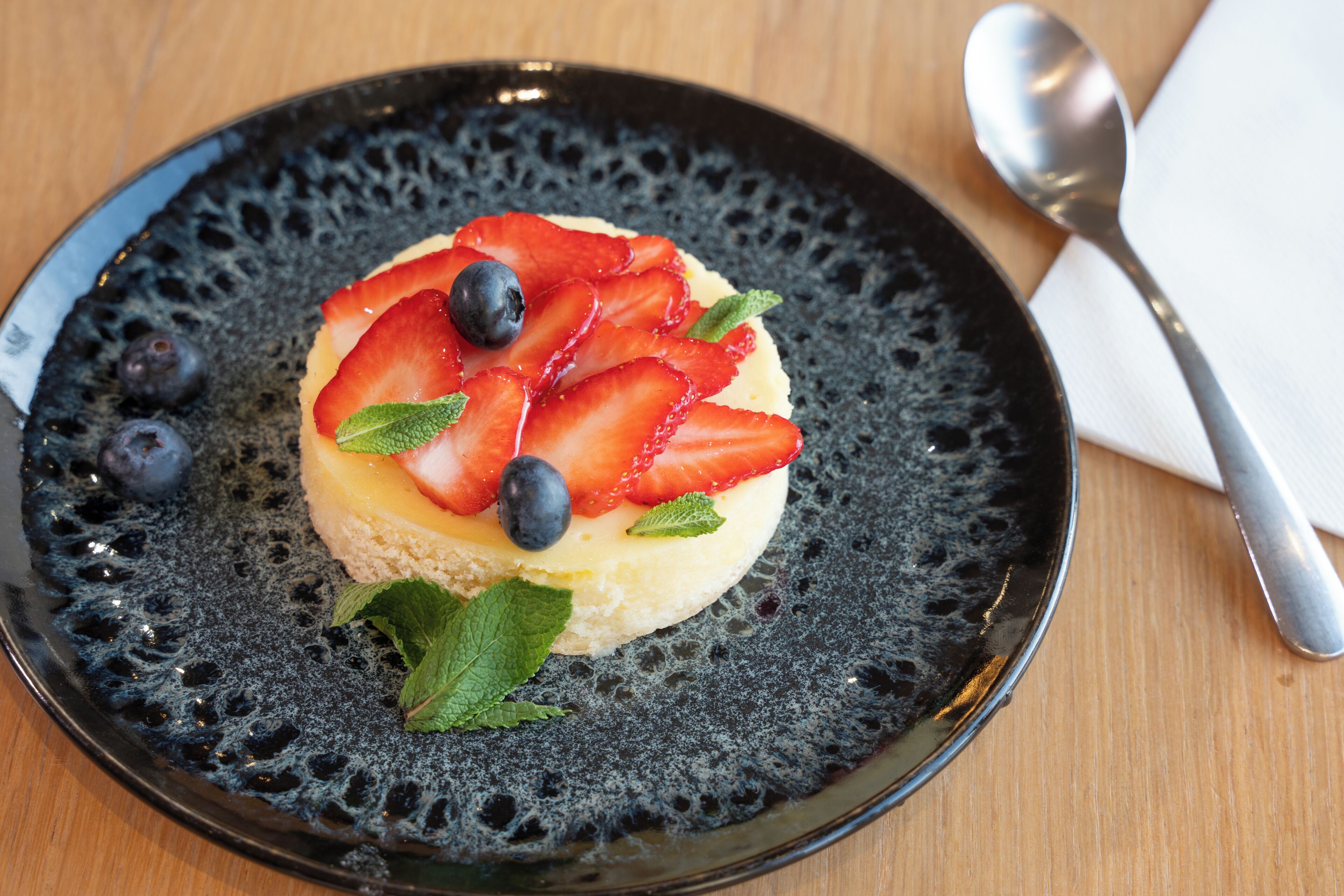 A dessert on a textured plate with a spoon and napkin beside it.