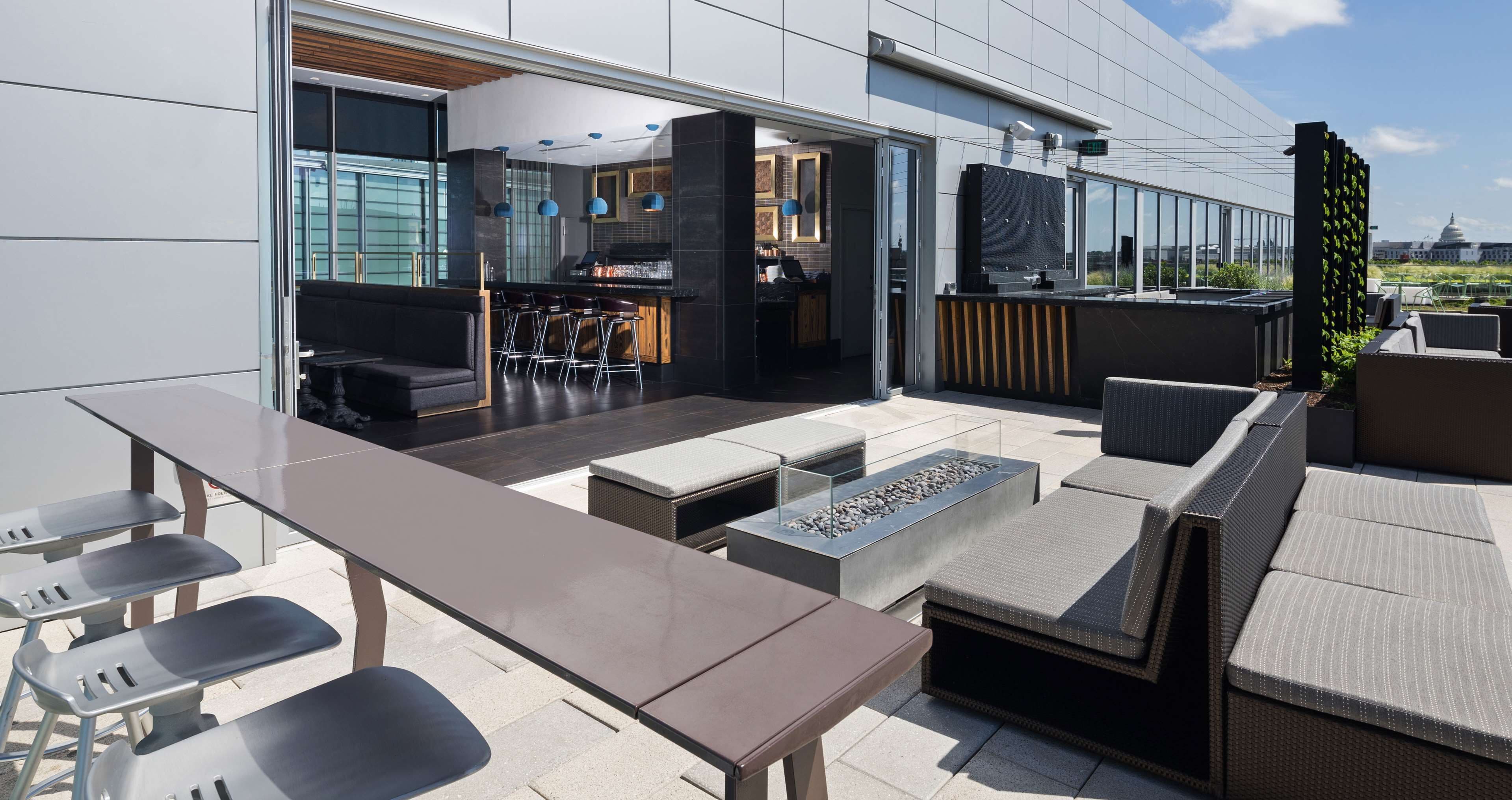 An outdoor patio with a bar area, seating, and a view of the cityscape.