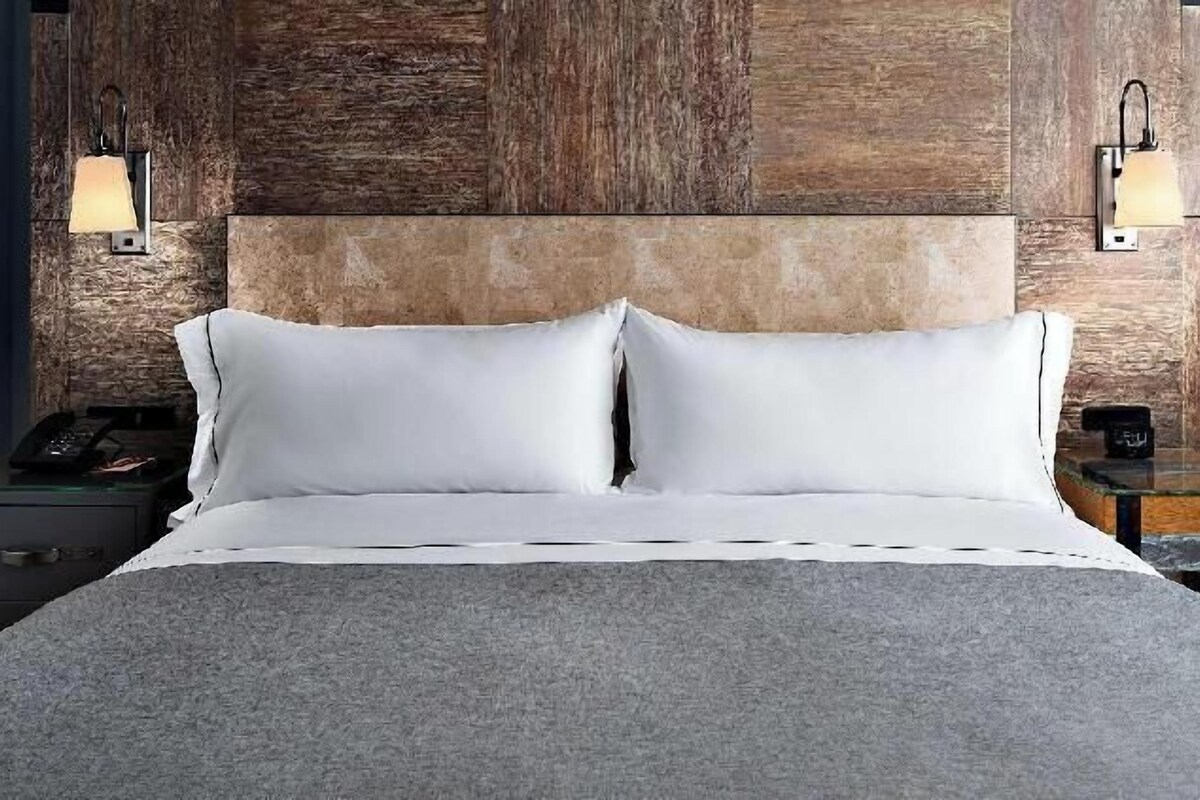 A hotel room with a bed, two bedside tables, a nightstand, and a wall-mounted lamp.