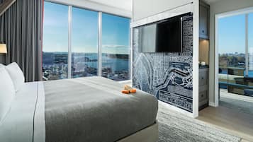 A modern hotel room with a large bed, a city view, a map on the wall, and a television.