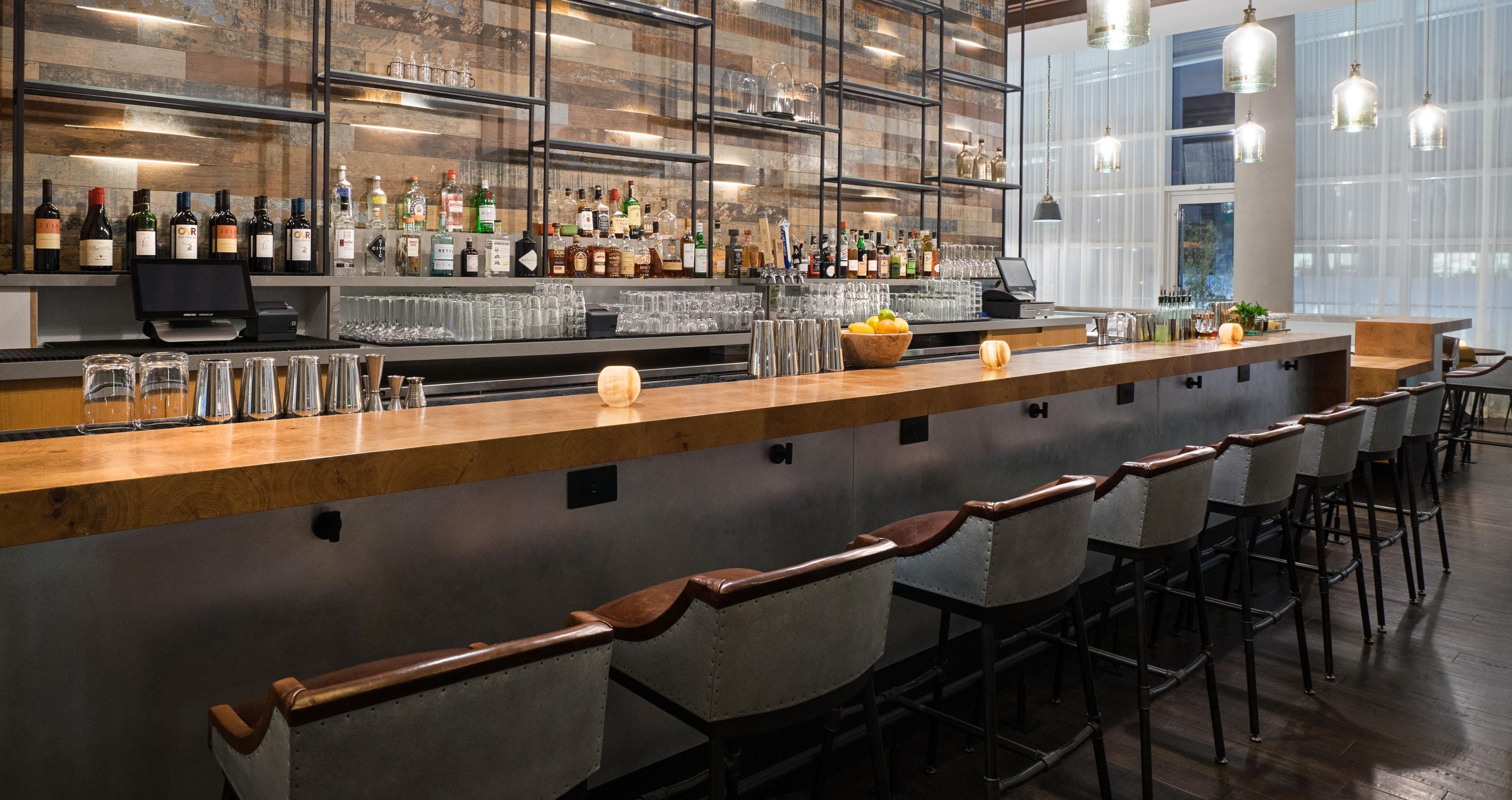 A bar area with a long counter, bar stools, and a variety of bottles and glasses.