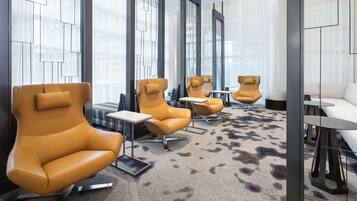 Un espace de détente moderne, avec des fauteuils en cuir et de petites tables, de grandes fenêtres et un tapis à motifs.
