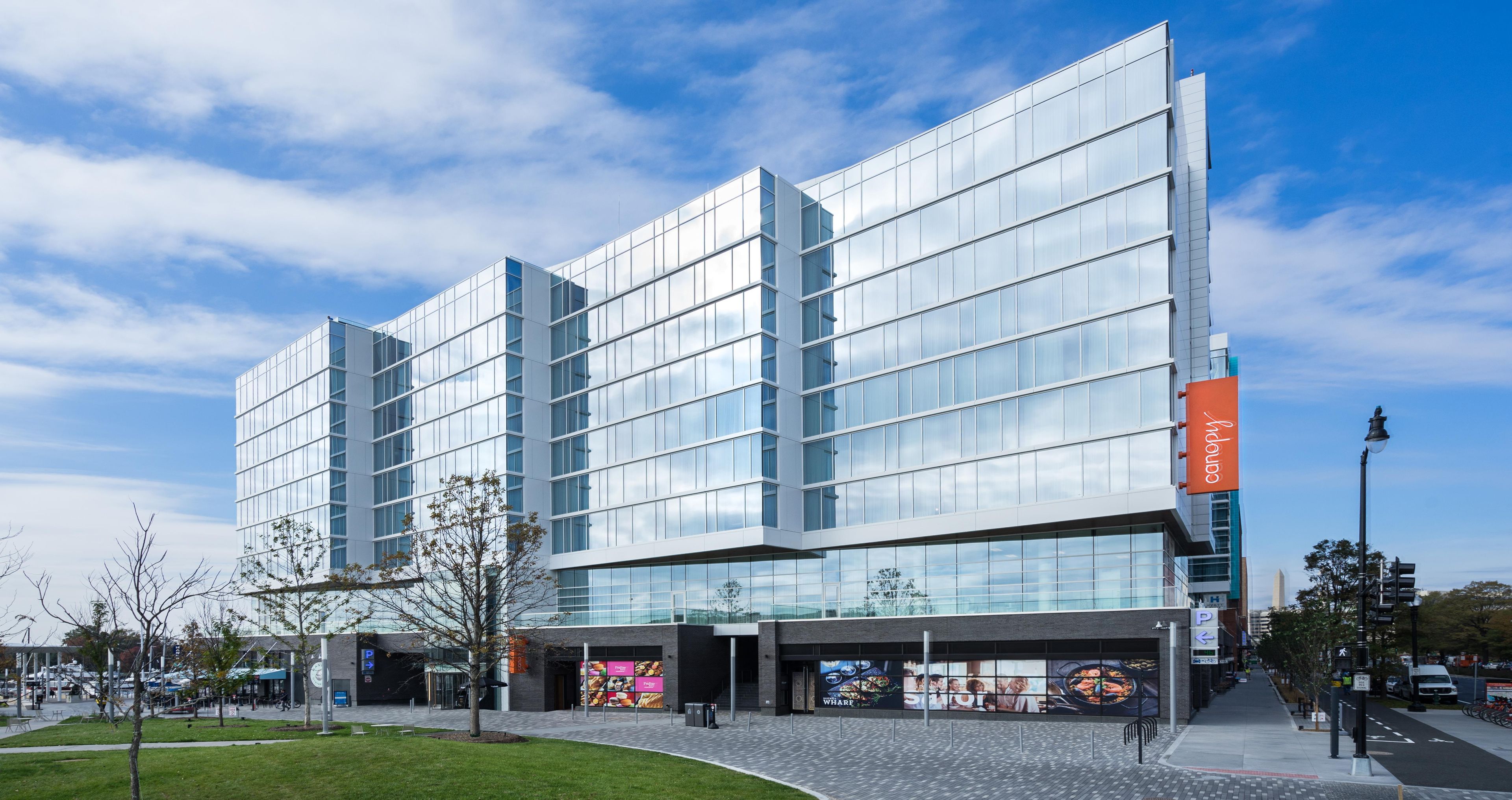 A modern building with a glass facade, a prominent orange sign, and a clear sky.