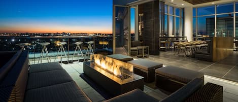 Una terraza en la azotea con una chimenea, asientos y vistas a la ciudad al anochecer.
