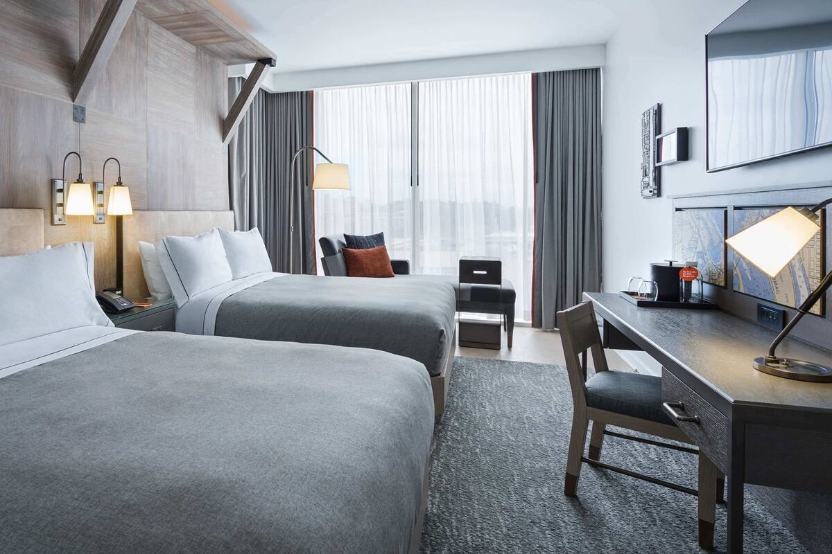 Habitación de hotel con dos camas, un escritorio, una silla, una lámpara, un teléfono y una ventana con cortinas.