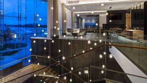 Eine moderne Hotellobby mit einer Glasstiege, einem Empfangsbereich und Blick auf die Stadtlandschaft.