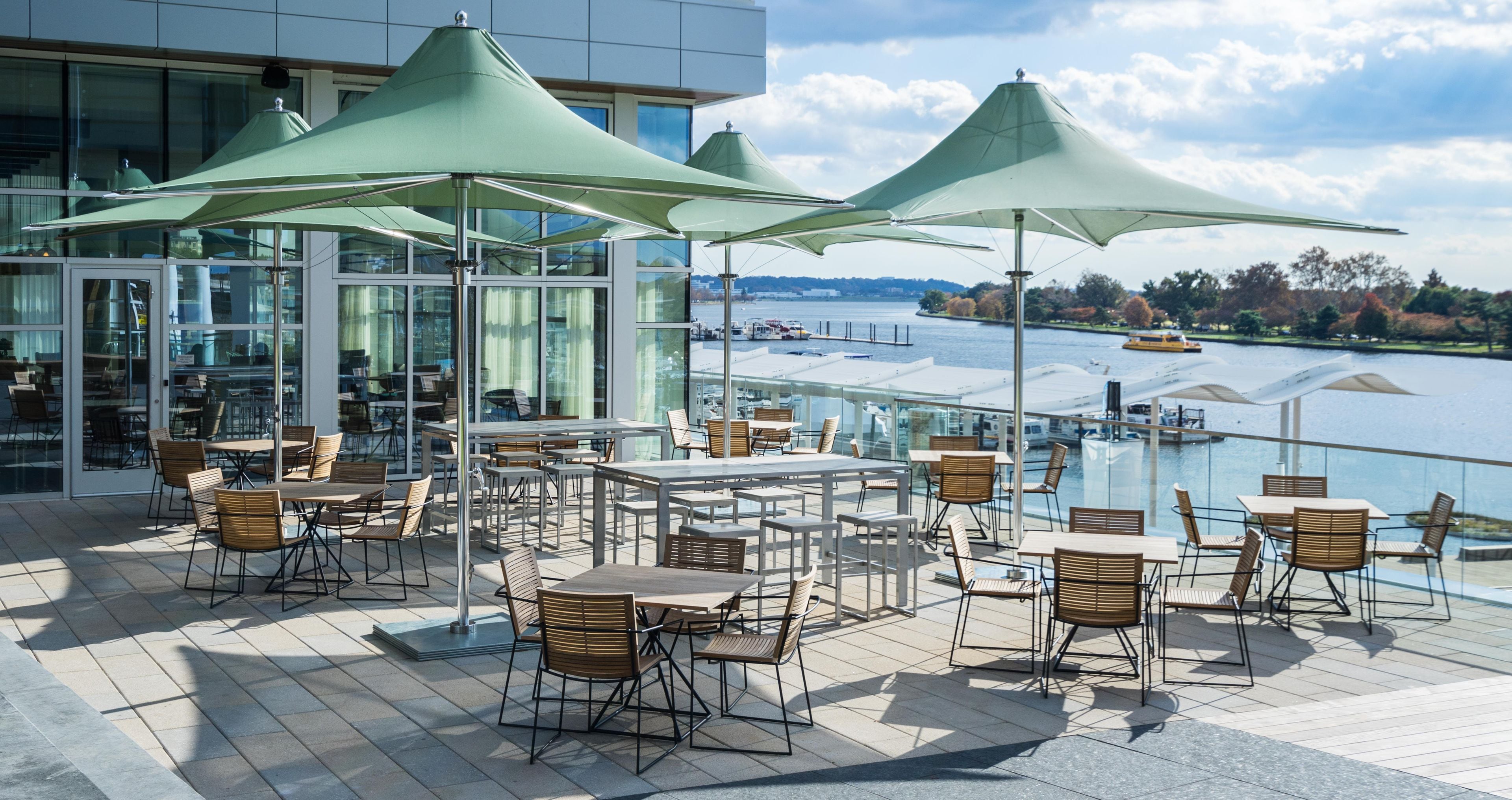 An outdoor terrace with tables and chairs, large umbrellas, and a view of a body of water.