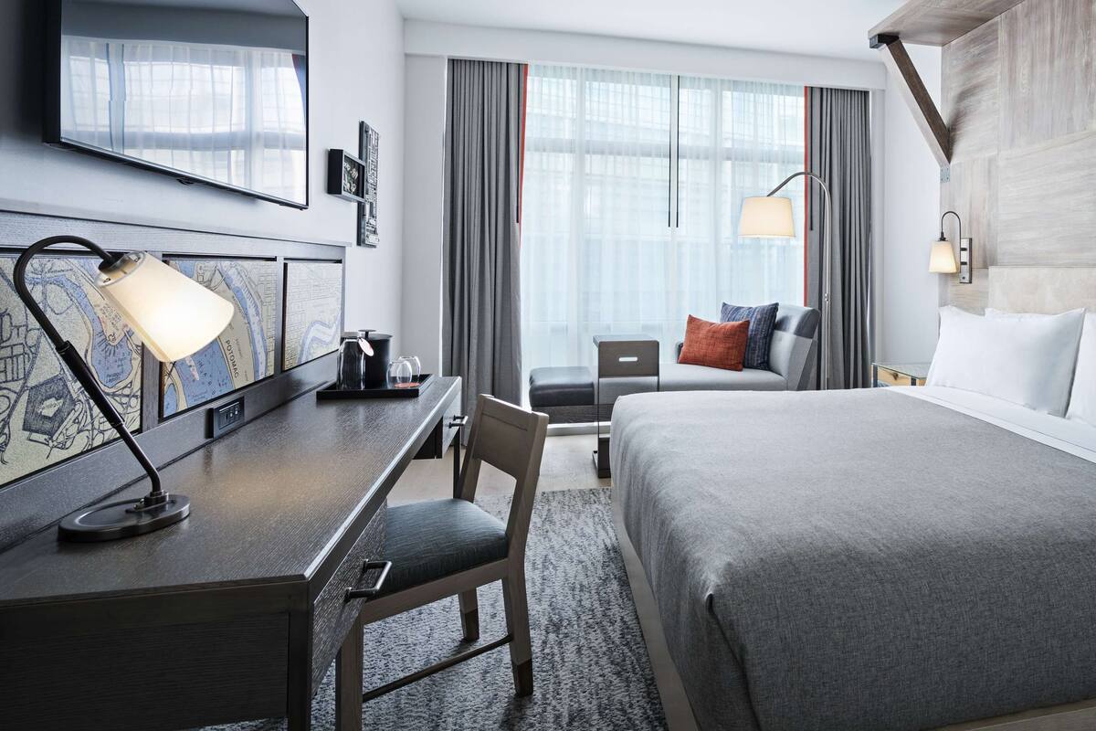 Hotellihuone, jossa on sänky, työpöytä, tuoli ja suuri ikkuna, jossa on verhot.