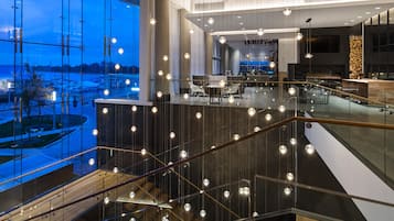 A modern interior with a glass railing overlooking a cityscape, a dining area with tables and chairs, and a fireplace.