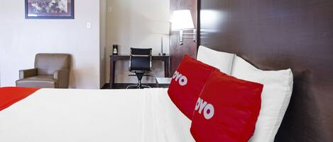 A hotel room with a large bed, a desk, a chair, and a lamp.