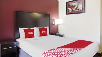 A hotel room with a large bed, two pillows with 'OYO' branding, a bedside table with a lamp, and a framed picture on the wall.