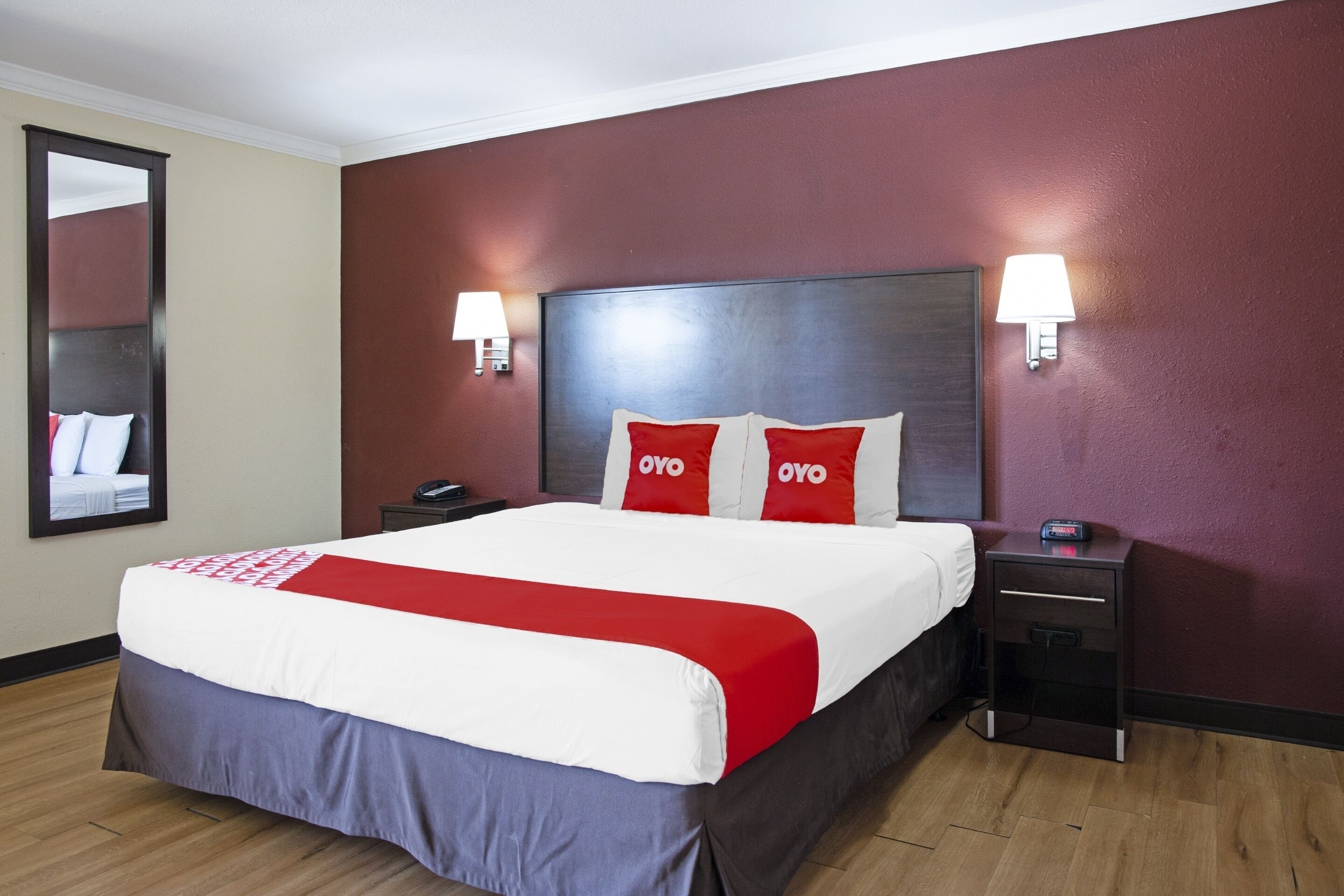 Habitación de hotel con una cama grande, dos mesitas de noche, un tocador, un espejo y dos lámparas de pared.