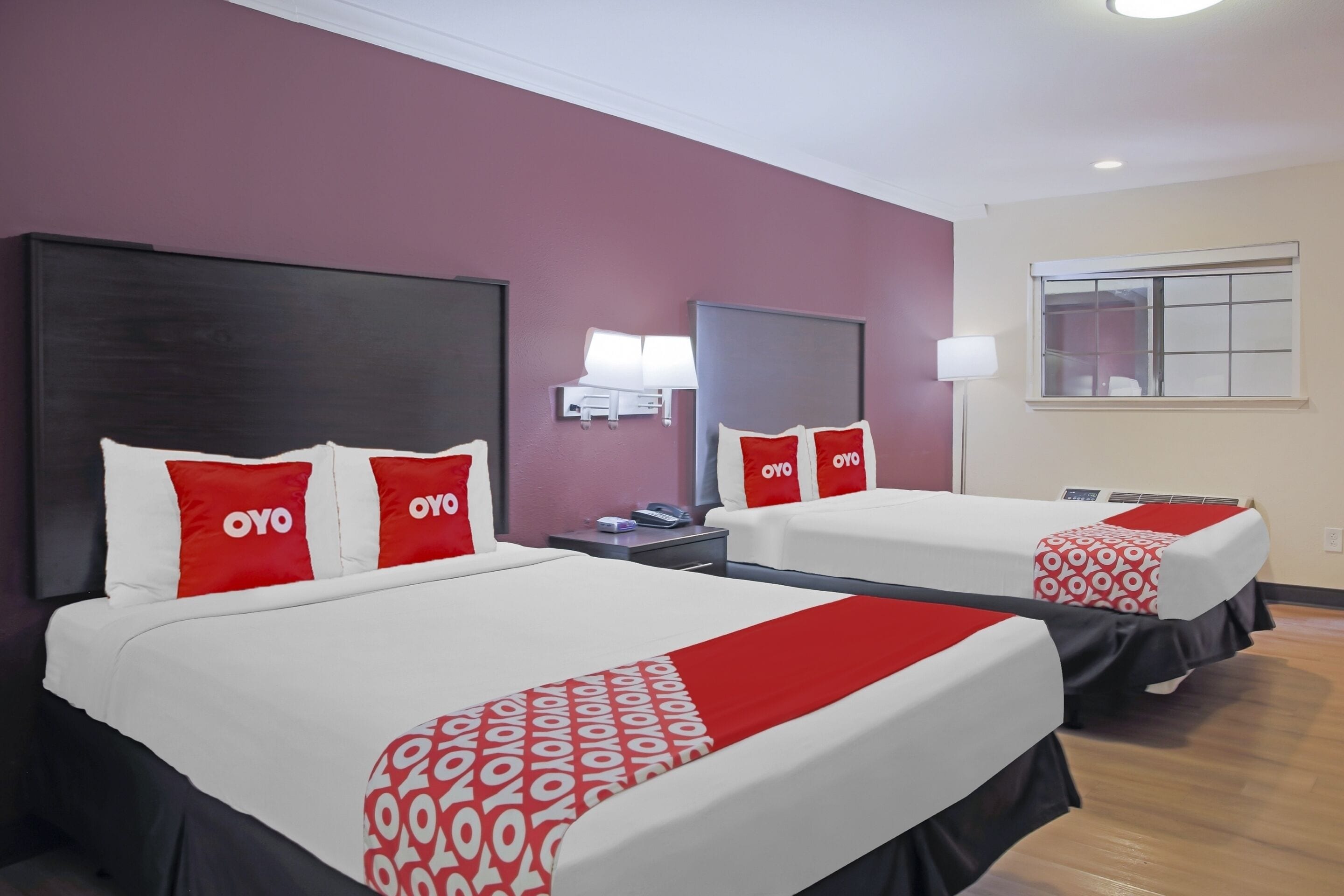 Une chambre d’hôtel avec deux lits, chacun doté de draps et d’oreillers rouges et blancs, une table de chevet, une lampe et une fenêtre avec des stores.