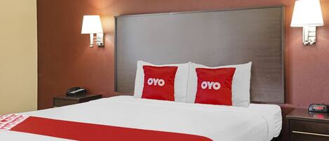 A hotel room with a large bed, two bedside lamps, a nightstand with a phone, and a digital clock.
