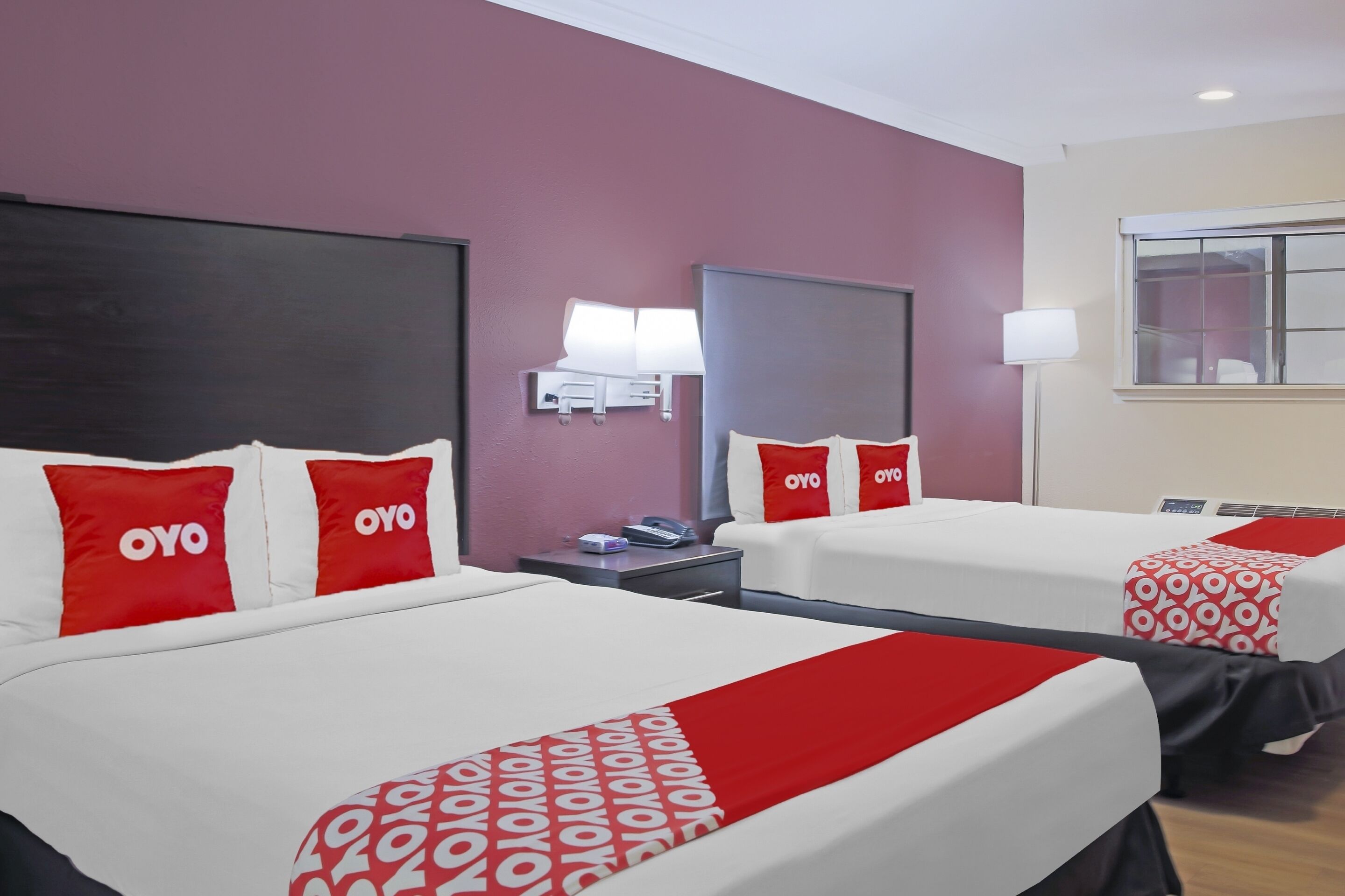 Habitación de hotel con dos camas, cada una con ropa de cama y almohadas con el logo 'OYO'.