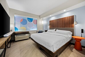 Een moderne hotelkamer met een groot bed, een bureau met een computer, een televisie en een houten wandpaneel.