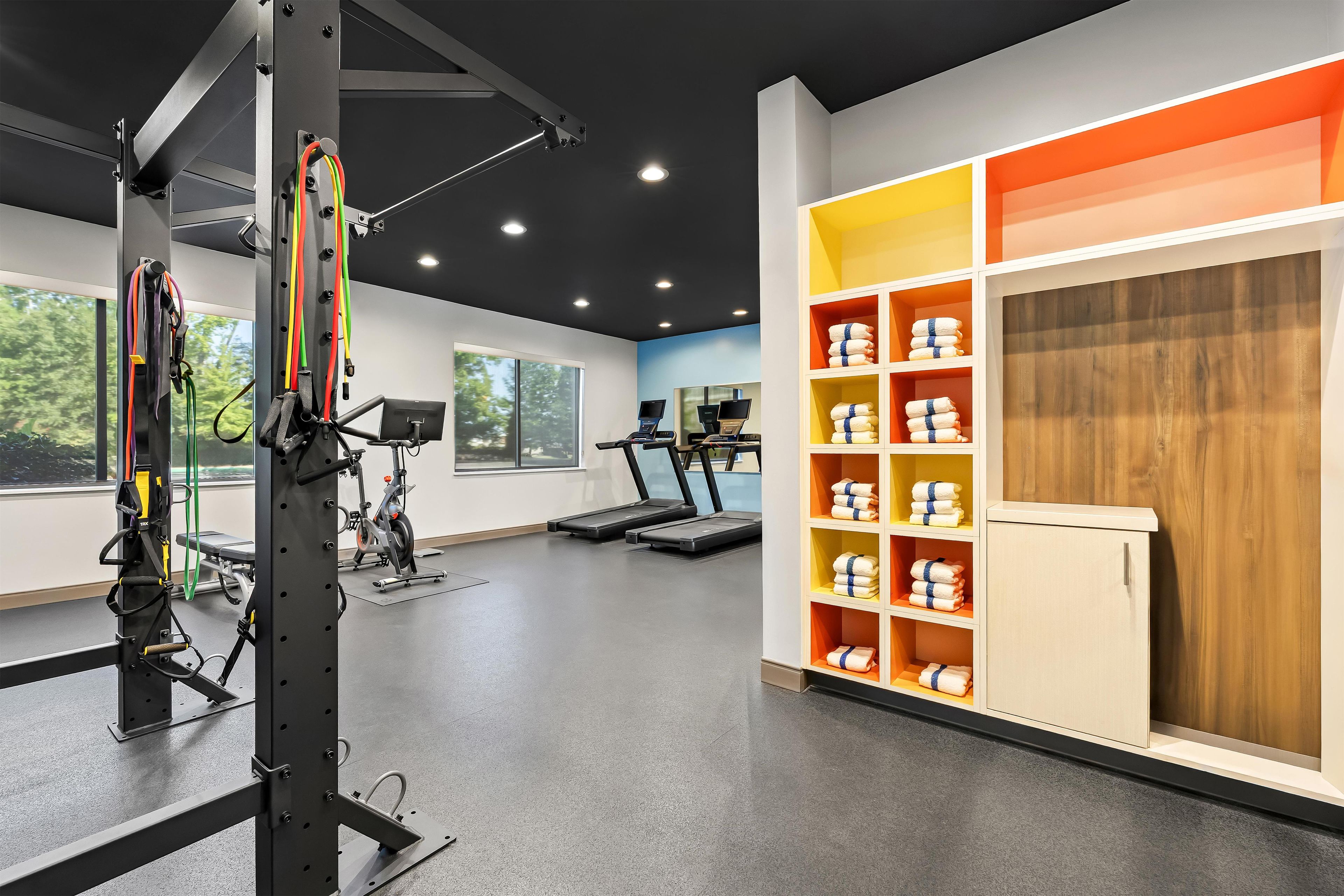 A gym with exercise equipment, a treadmill, and a wall with shelves of towels.