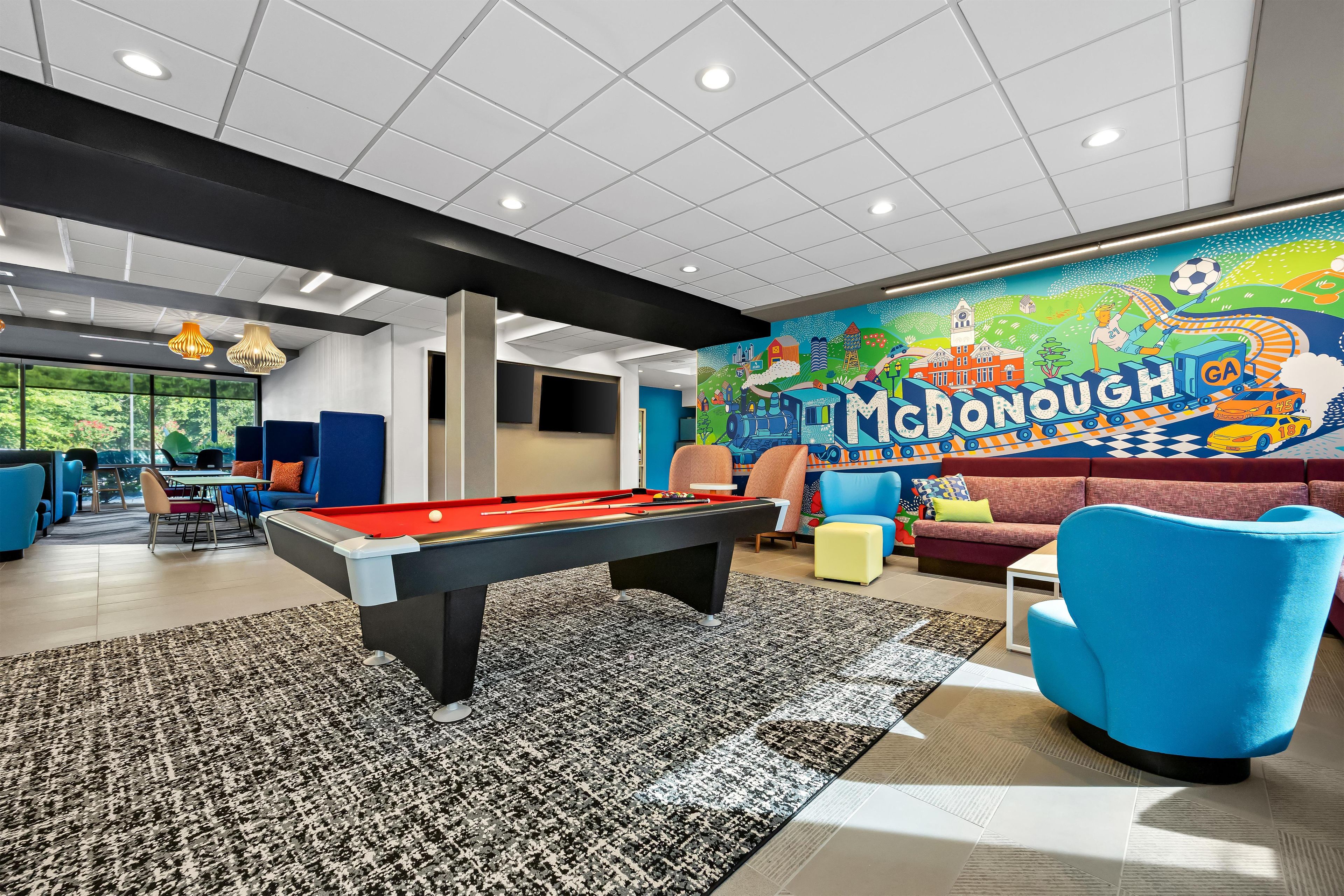 A pool table in a room with a colorful mural, blue chairs, and a sofa.