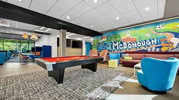 A pool table in a room with a colorful mural, blue chairs, and a sofa.