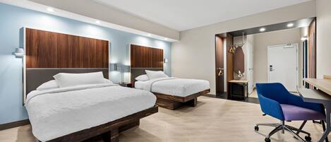 Ein Hotelzimmer mit zwei Betten, einem Schreibtisch mit Stuhl und einem durchgehenden Türspalt einsehbarer Badezimmer.