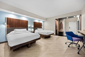 Una habitación de hotel con dos camas, un escritorio con una silla y un baño visible a través de una puerta abierta.