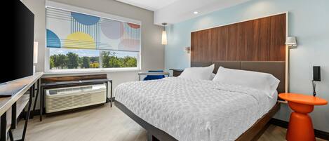 Una habitación de hotel moderna con una cama grande, un escritorio, un calentador, una ventana con vistas y un cabecero de madera.