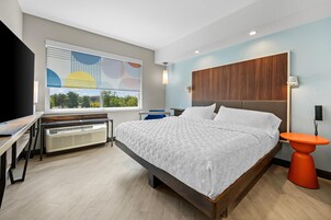 Una habitación de hotel moderna con una cama grande, un escritorio, un calentador, una ventana con vistas y un cabecero de madera.