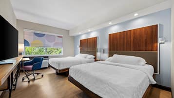 A hotel room with two beds, a desk, a chair, and a television.
